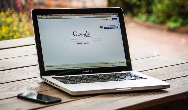 Iphone und Mac mit geöffneter Google Startseite auf einem Holztisch